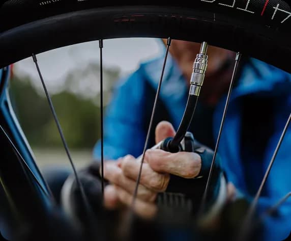 A mechanic inflating a bicycle tyre with a portable pump during a roadside repair.