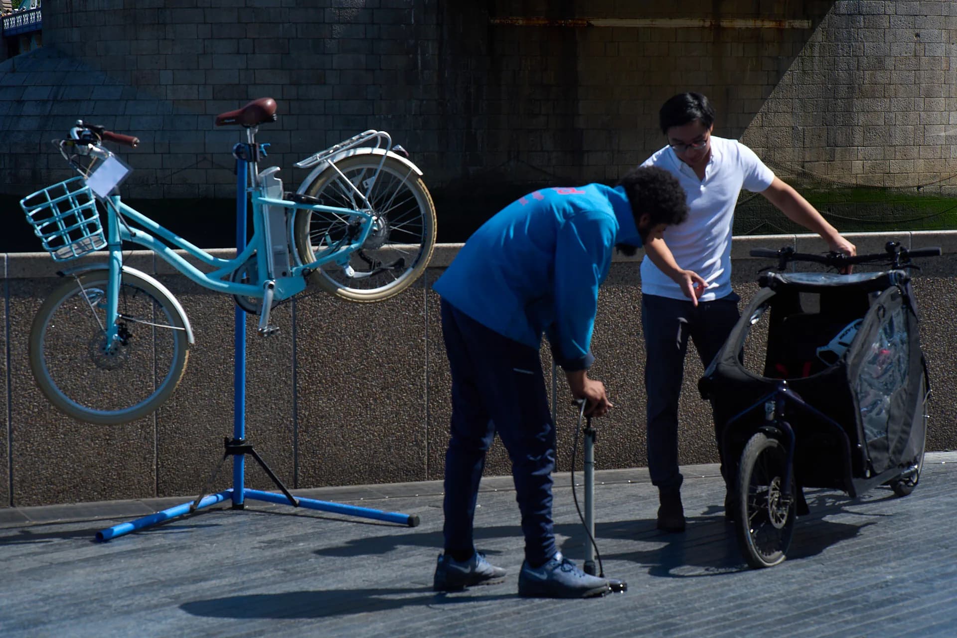 A Tyred mechanic pumping up a tyre beside a bike on a repair stand in London.