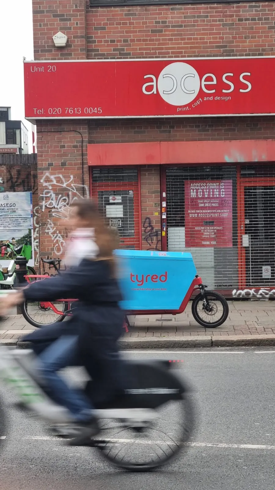 A commuter cycling past a parked Tyred cargo bike on a London street.