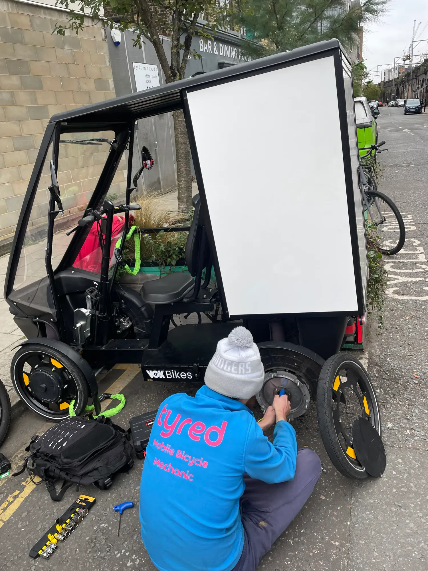 A Tyred mechanic repairing a VOK cargo e-bike at the roadside in London.