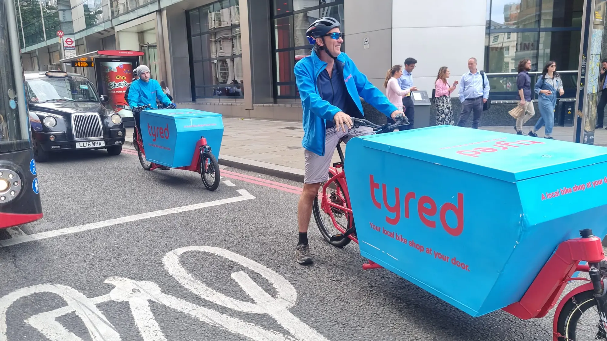 Two Tyred mechanics riding branded cargo bikes through central London.