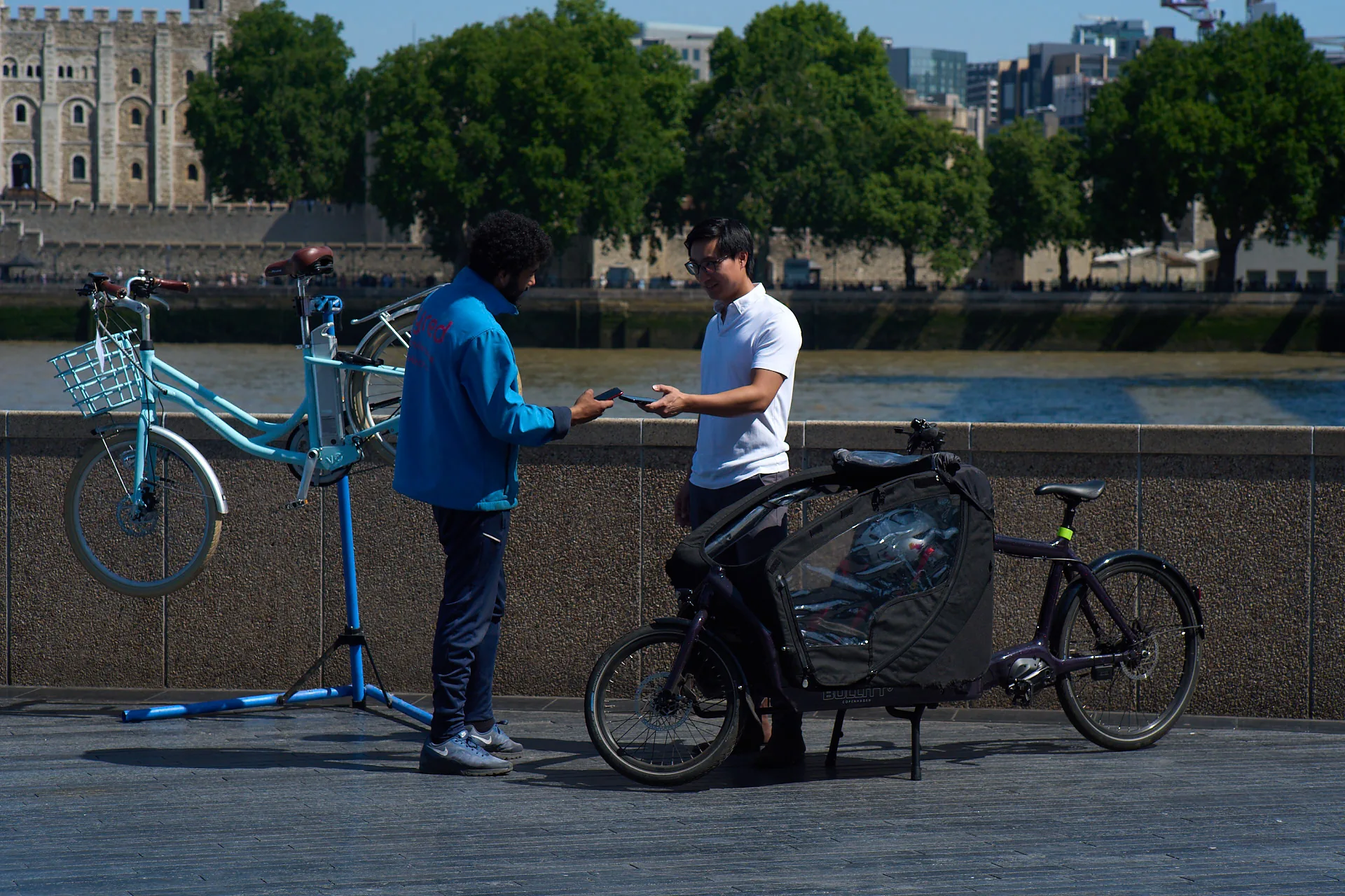 A Tyred mechanic helping a customer by the Thames, with the Tower of London in the background.