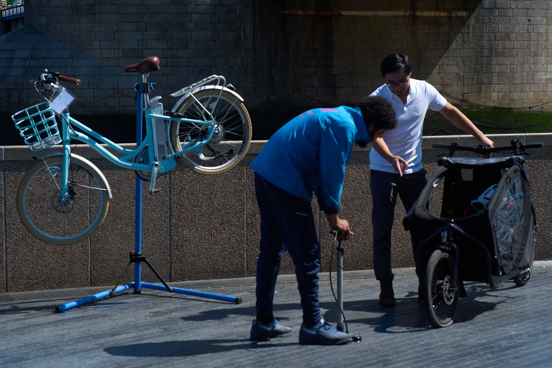 A Tyred mechanic pumping up a tyre beside a bike on a repair stand in London.