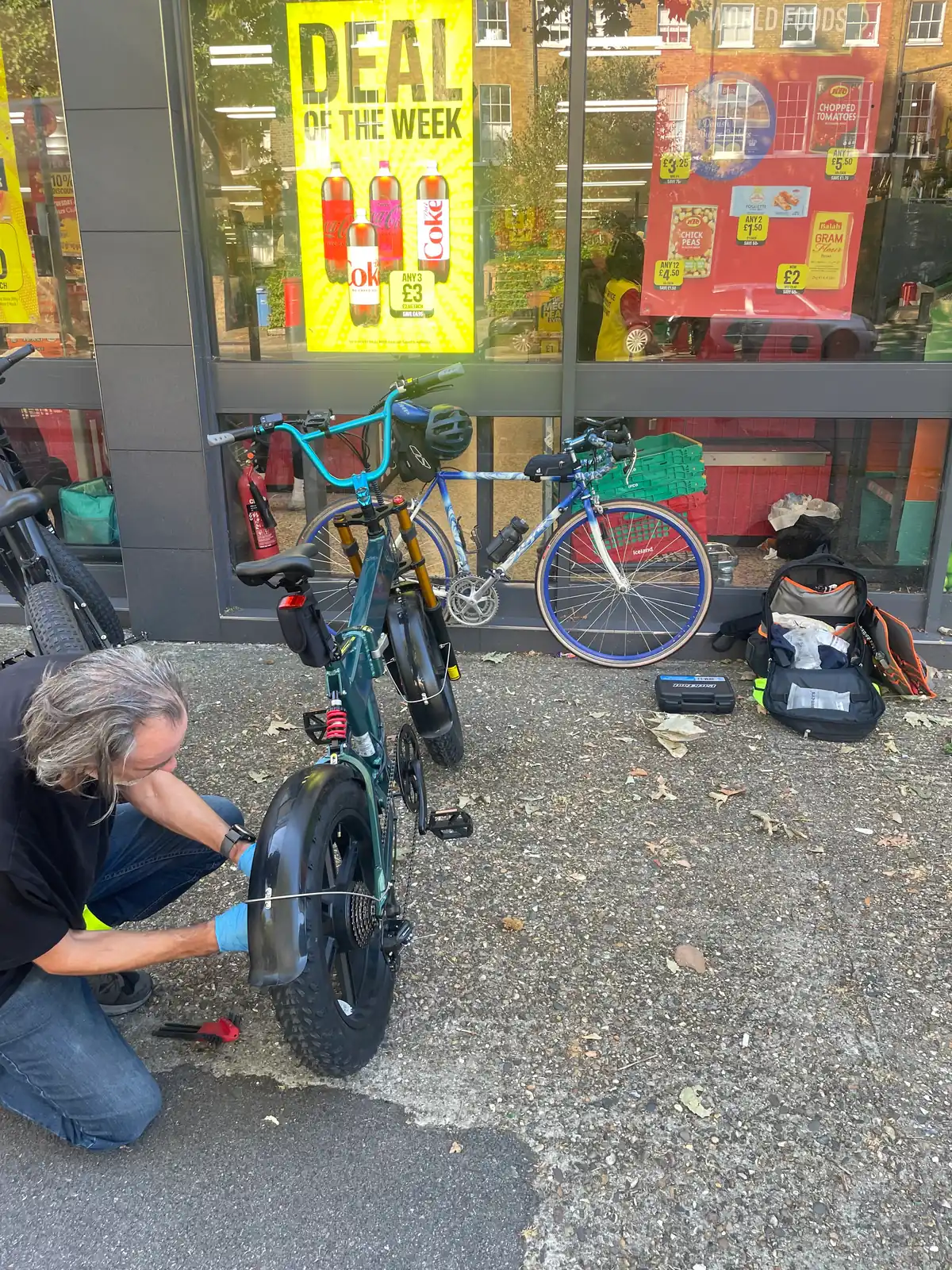 A Tyred mechanic repairing an e-bike on a London pavement.